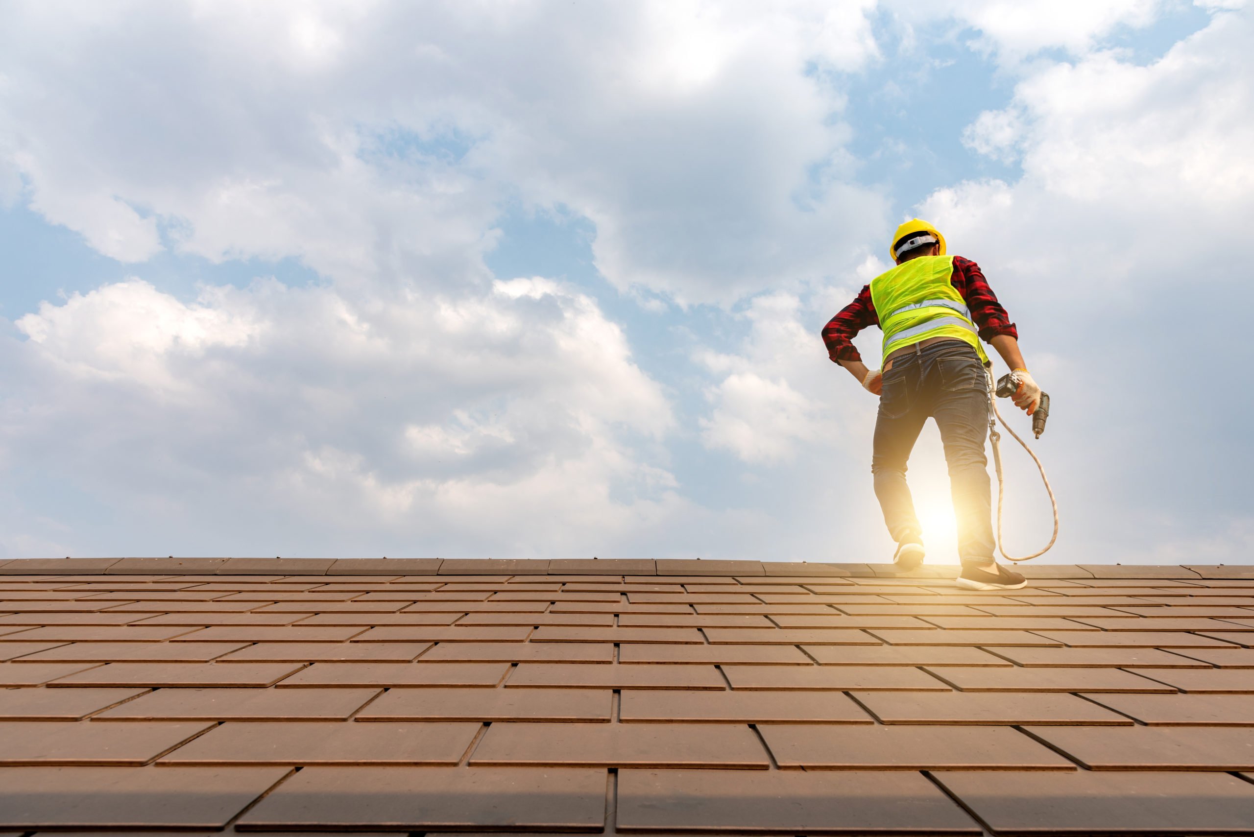 Construction workers lay a roof with a nail gun to develop a large commercial building.